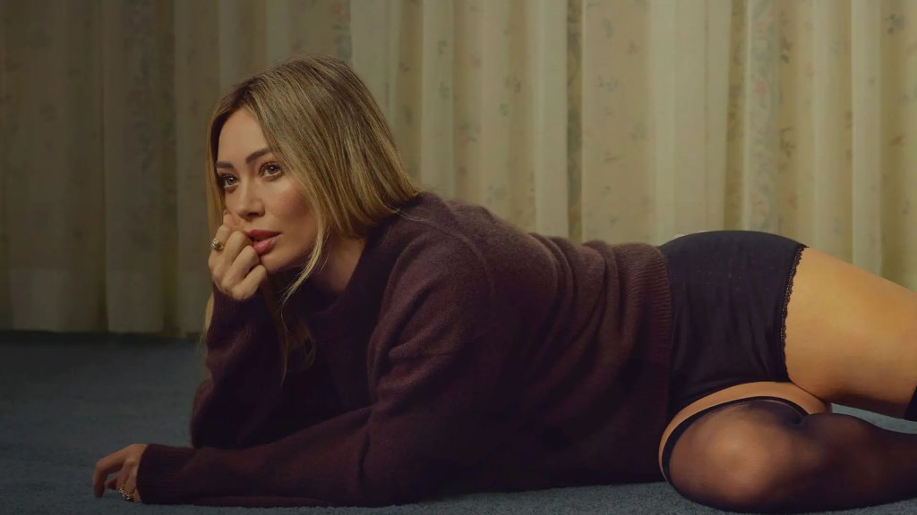 A woman is lying on her side on a carpeted floor, wearing a loose sweater and black underwear, with her head resting on her hand in Williamson County, Tennessee.