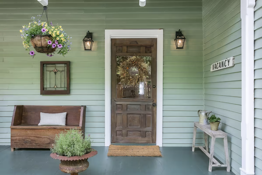 A charming porch with a wooden bench, hanging flower basket, and a rustic door adorned with a wreath, inviting visitors to enjoy the peaceful surroundings in Williamson County, Tennessee.