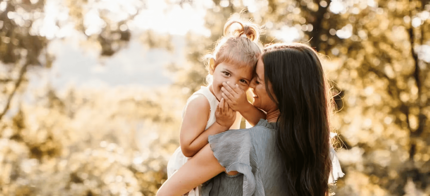 A woman with long dark hair tenderly holds a young child with blonde hair in a lush, green forest, both sharing a joyful moment in Williamson County, Tennessee.