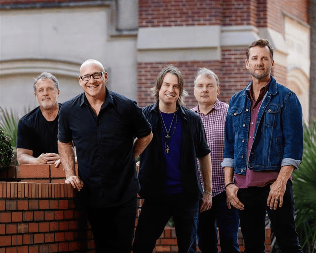 A group of five men, dressed in casual attire, stand together in front of a brick wall with greenery in the background in Williamson County, Tennessee.