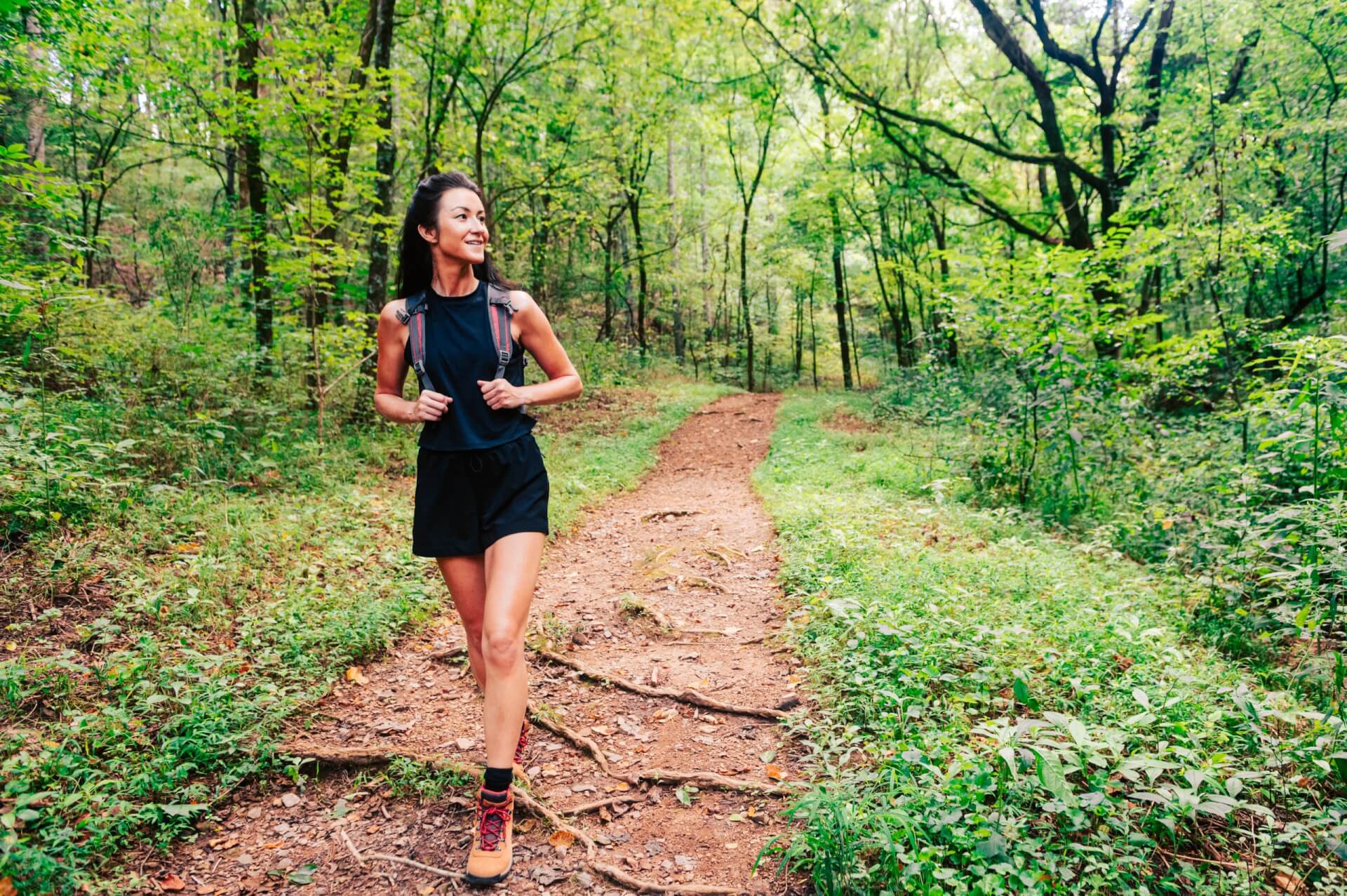 Personas Testing A woman in athletic attire smiles as she walks along a dirt path through a lush, green forest in Williamson County, Tennessee.