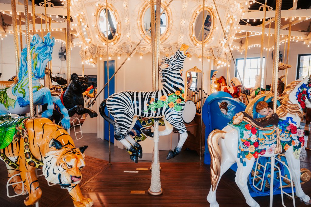 A vibrant carousel featuring a menagerie of elaborately decorated horses, a zebra, a tiger, and a black panther, all illuminated by a dazzling array of golden lights and surrounded by ornate mirrors in Williamson County, Tennessee.