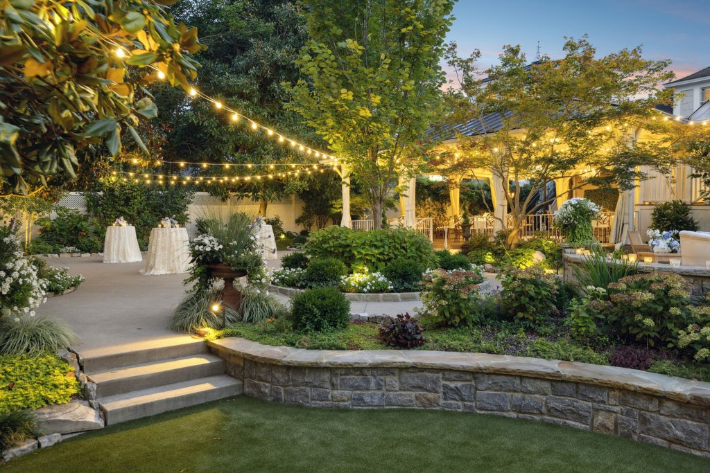 A beautifully landscaped garden with string lights, white tables, and lush greenery creates a serene outdoor event space in Williamson County, Tennessee.