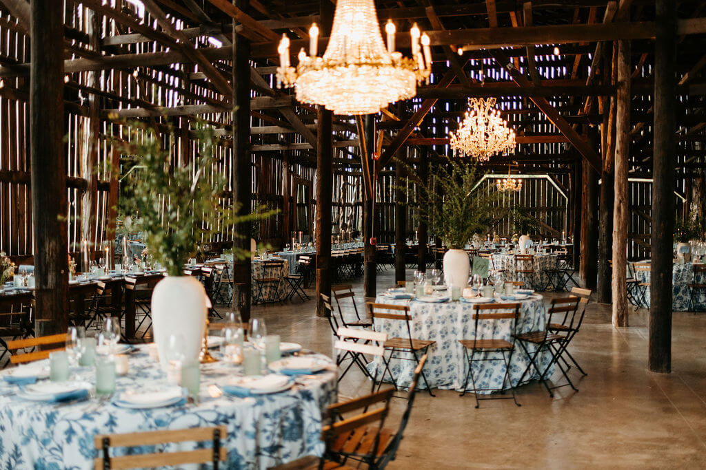 An elegant wedding reception in a rustic barn with chandeliers, floral centerpieces, and blue and white tablecloths in Williamson County, Tennessee.