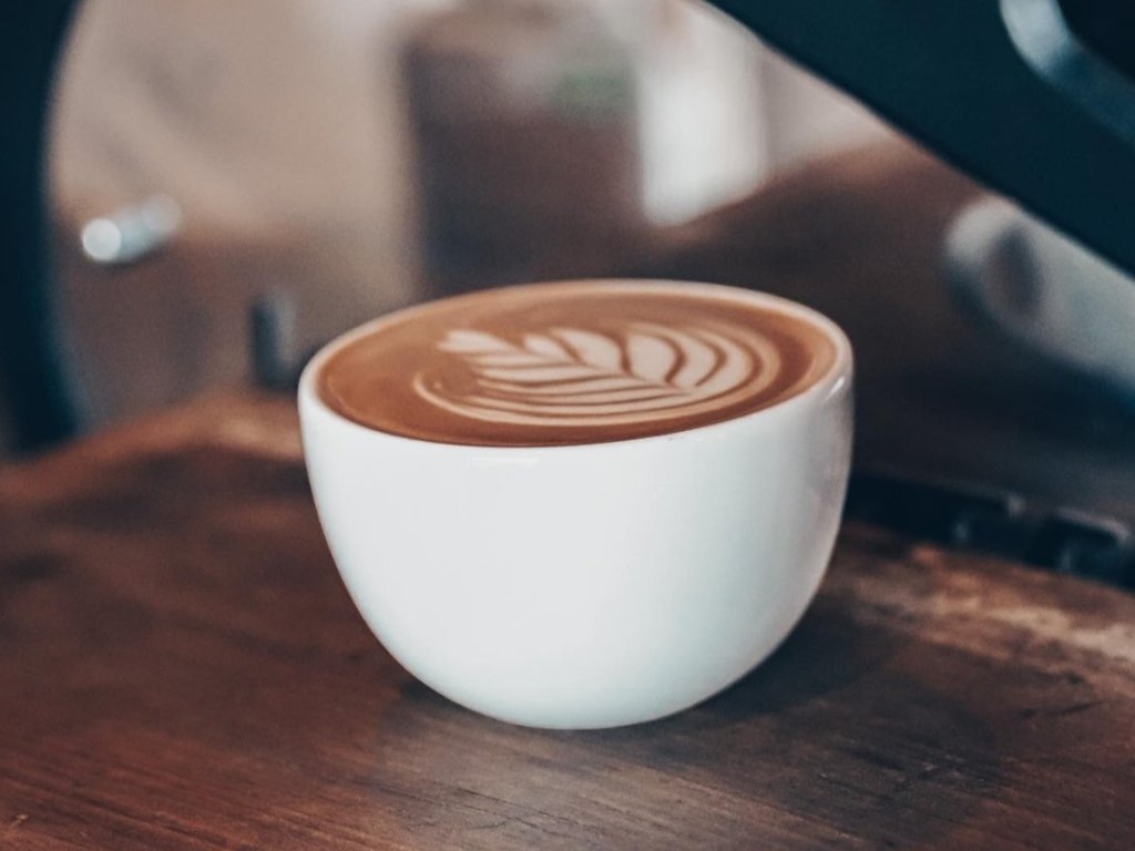 A beautifully crafted latte with intricate leaf-shaped foam art sits in a white ceramic cup on a wooden surface in Williamson County, Tennessee.