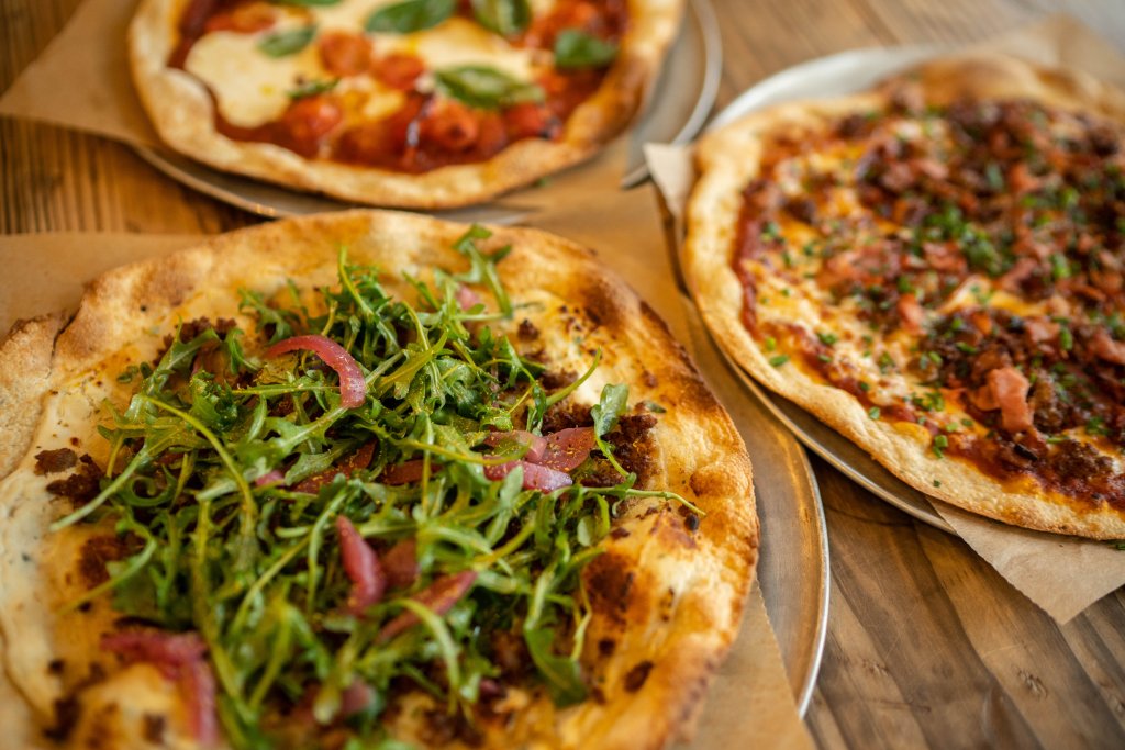 Three gourmet pizzas with unique toppings displayed on metal trays on a rustic wooden table in Williamson County, Tennessee.