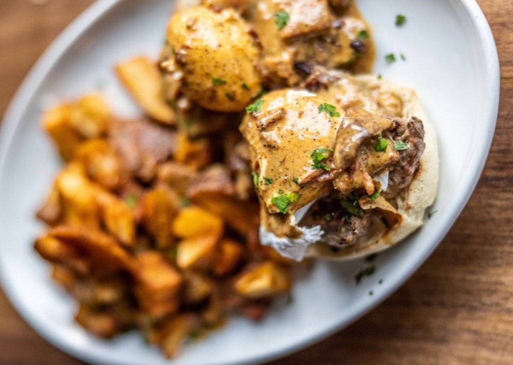 A hearty breakfast featuring eggs benedict with beef and mushrooms, served alongside crispy roasted potatoes on a wooden table in Williamson County, Tennessee.
