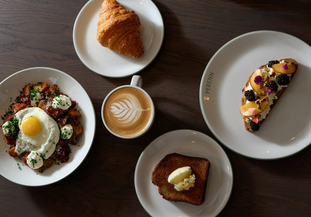 A variety of breakfast items including a croissant, a cup of coffee with latte art, a plate of eggs with potatoes and herbs, and two slices of toast with different toppings in Williamson County, Tennessee.