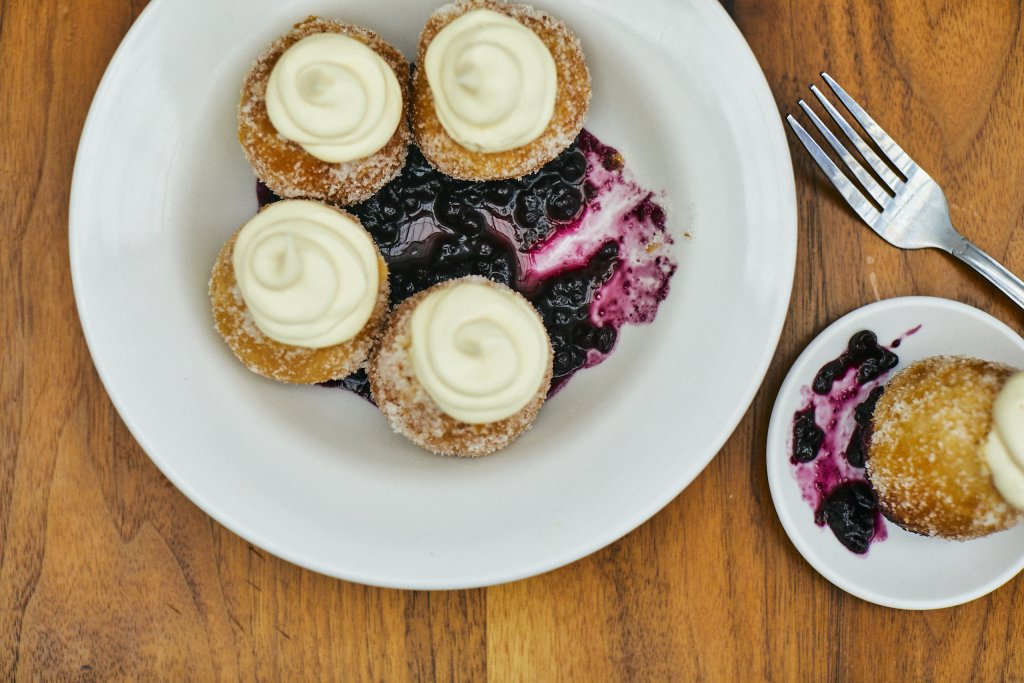 Four sugar-coated doughnut holes topped with swirls of whipped cream and served with a side of blueberry compote on a white plate in Williamson County, Tennessee.