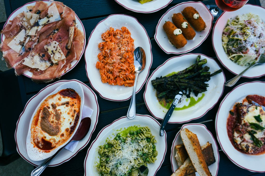 A variety of Italian dishes including cured meats, pasta, fried appetizers, salads, and desserts are artfully arranged on a dark table in Williamson County, Tennessee.