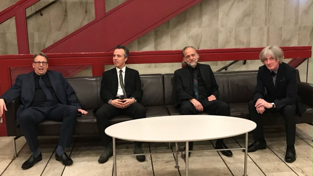 Four men in formal attire sit on a black leather couch in a modern lobby with a red staircase in the background in Williamson County, Tennessee.