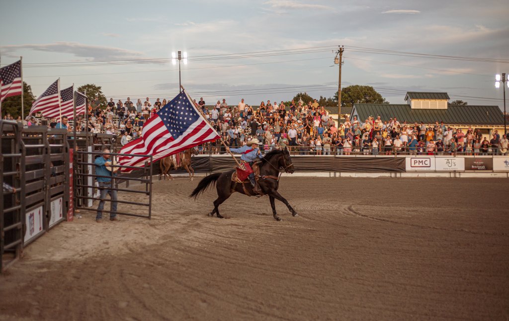 A cowboy gallops around a rodeo arena, waving an American flag, as a large crowd cheers from the stands in Williamson County, Tennessee.