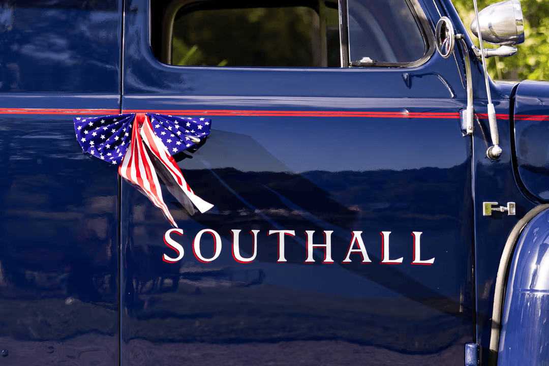 A vintage blue truck with 'SOUTHALL' written on its side, adorned with an American flag ribbon in Williamson County, Tennessee.