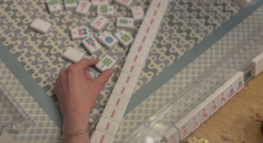 A hand is carefully placing a Mahjong tile on a patterned board, surrounded by various other tiles in Williamson County, Tennessee.