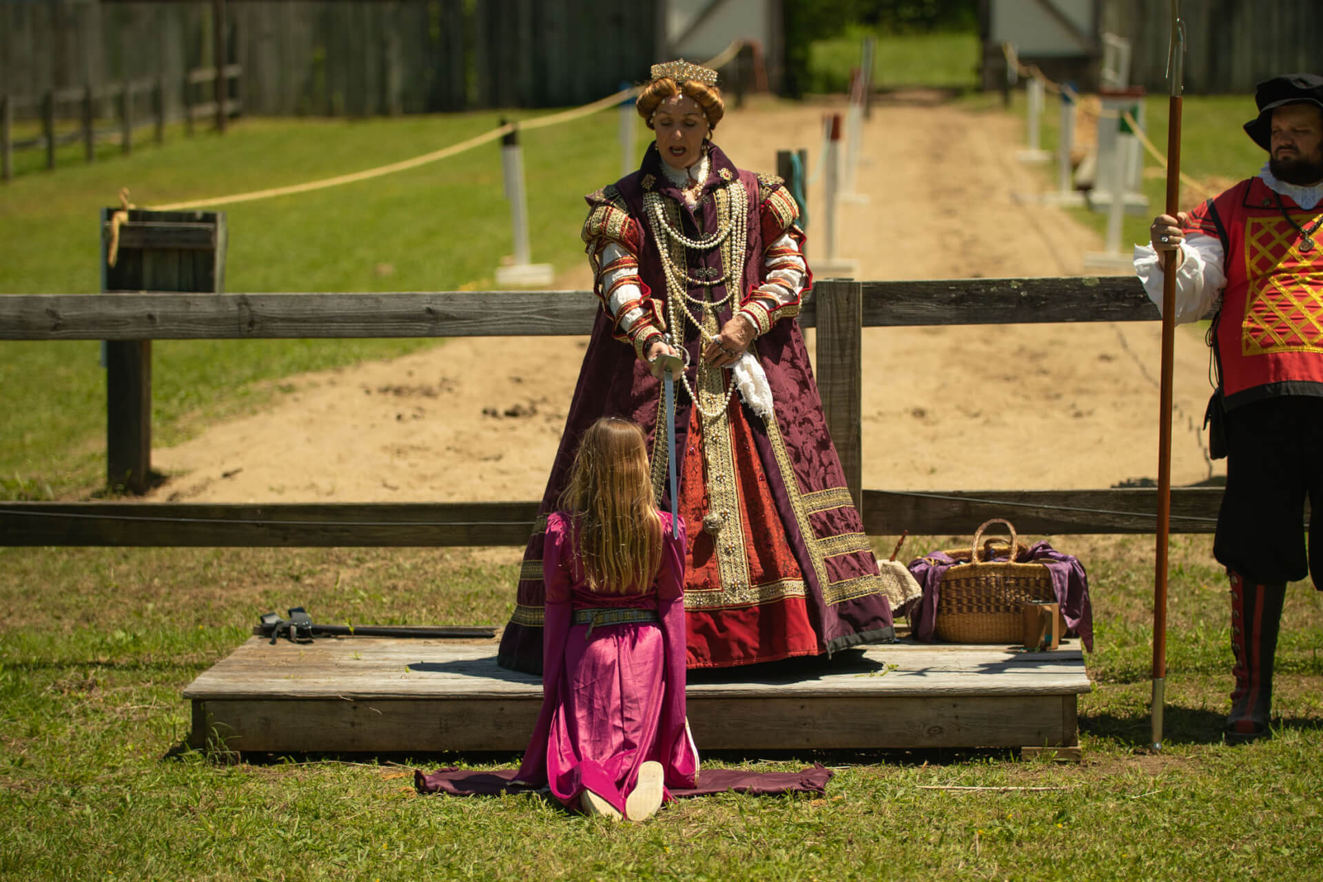 Tennessee Renaissance Festival A woman dressed in a richly embroidered Renaissance gown kneels before a figure in regal attire, offering a sword as part of a historical reenactment ceremony in Williamson County, Tennessee.