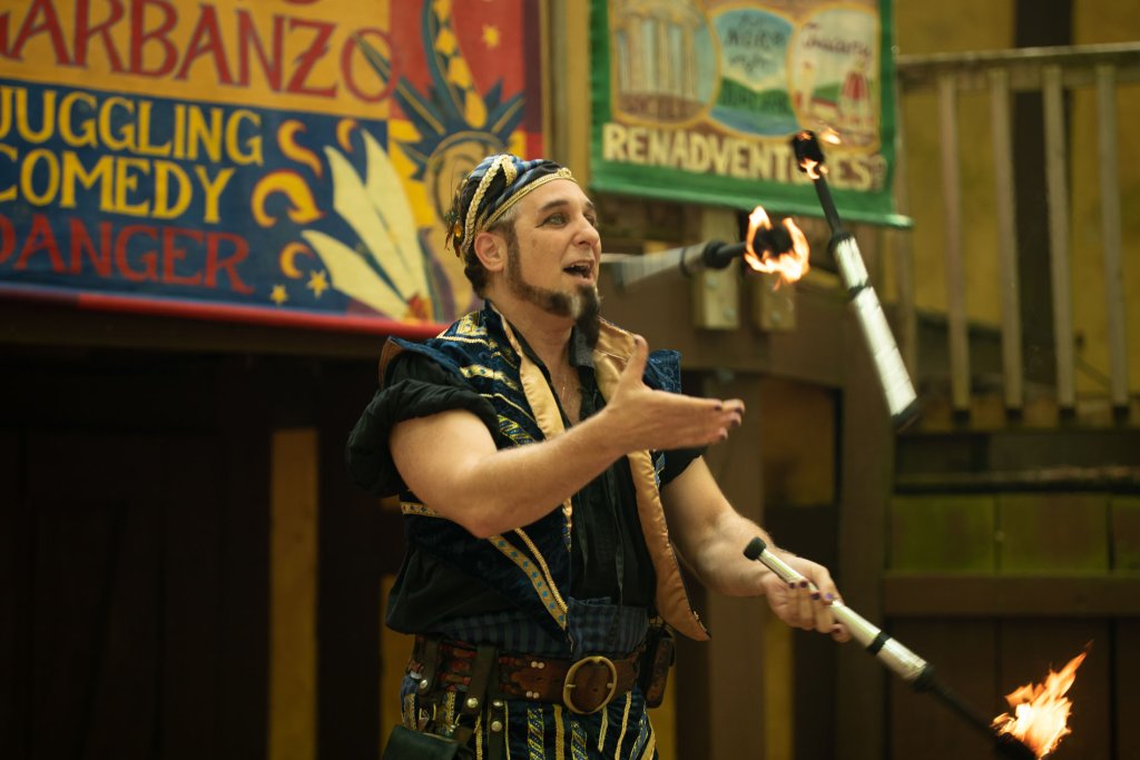 Tennessee Renaissance Festival A man dressed in a colorful, medieval-inspired outfit juggles three flaming torches with skill and flair in Williamson County, Tennessee.