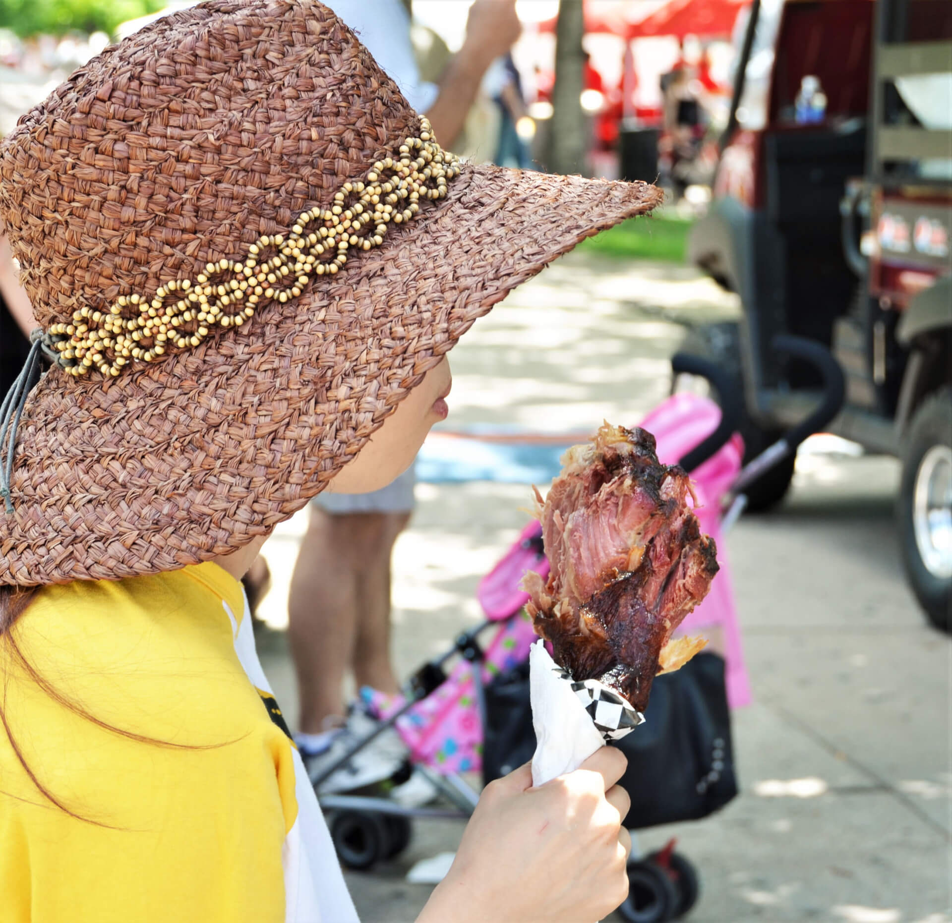 Tennessee Renaissance Festival A young girl wearing a wide-brimmed straw hat with a beaded band enjoys a large, juicy drumstick at an outdoor event in Williamson County, Tennessee.