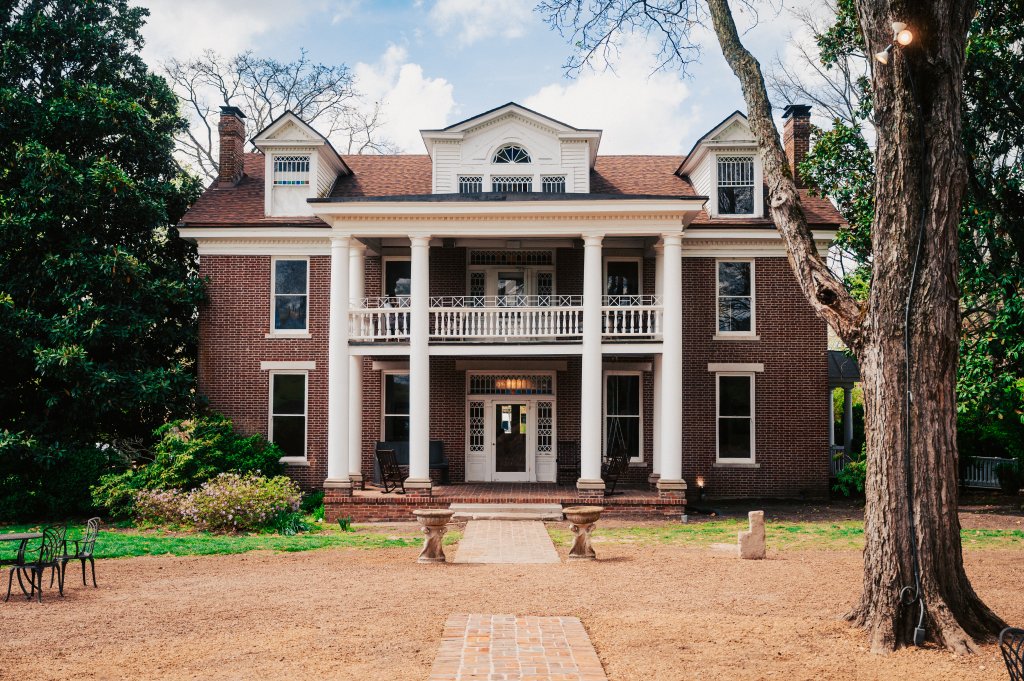 A stately two-story brick mansion with a grand front porch supported by white columns, set amidst lush greenery and a large tree in Williamson County, Tennessee.