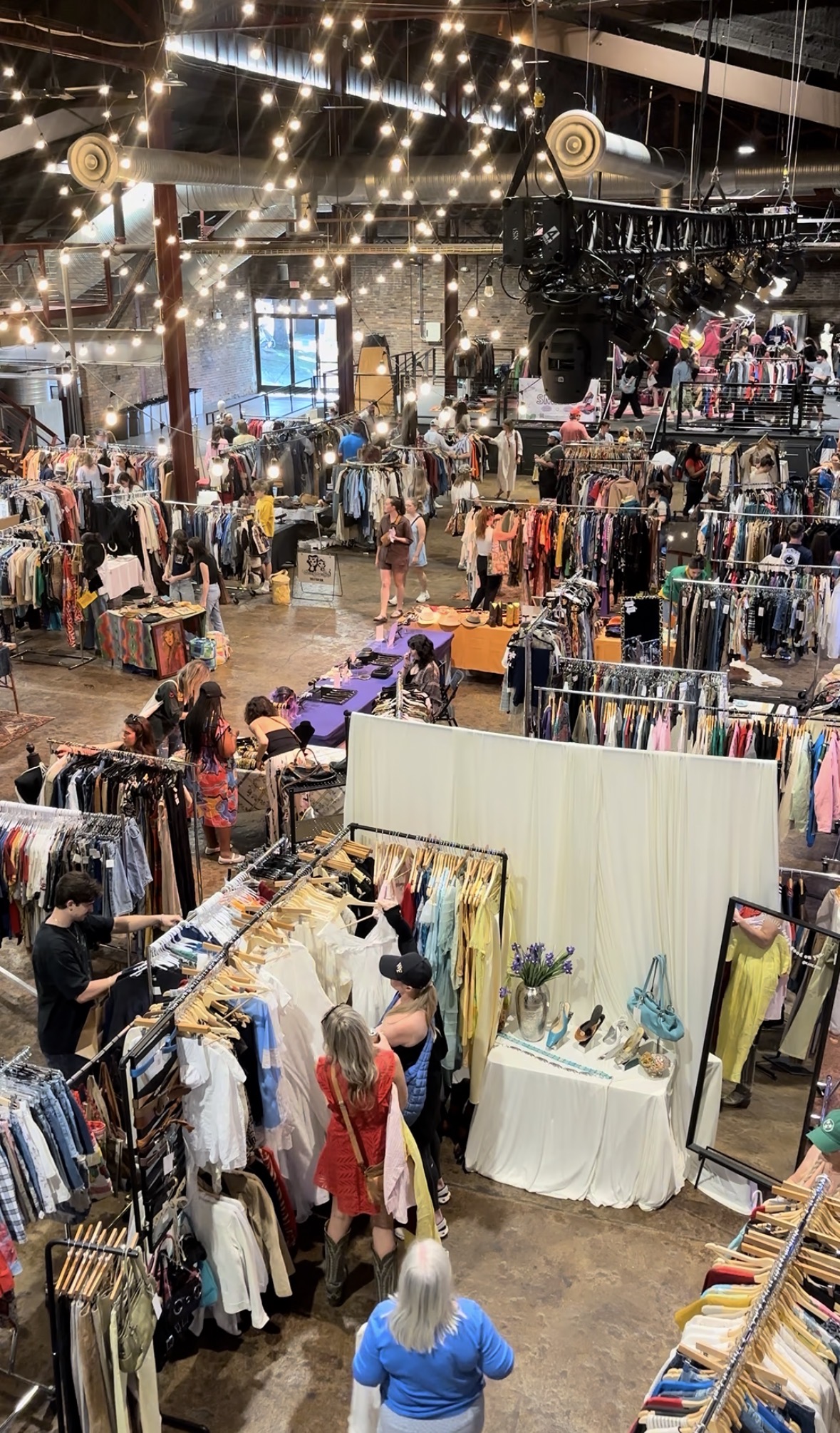 A bustling indoor flea market filled with rows of clothing racks, tables displaying various items, and shoppers browsing the merchandise in Williamson County, Tennessee.