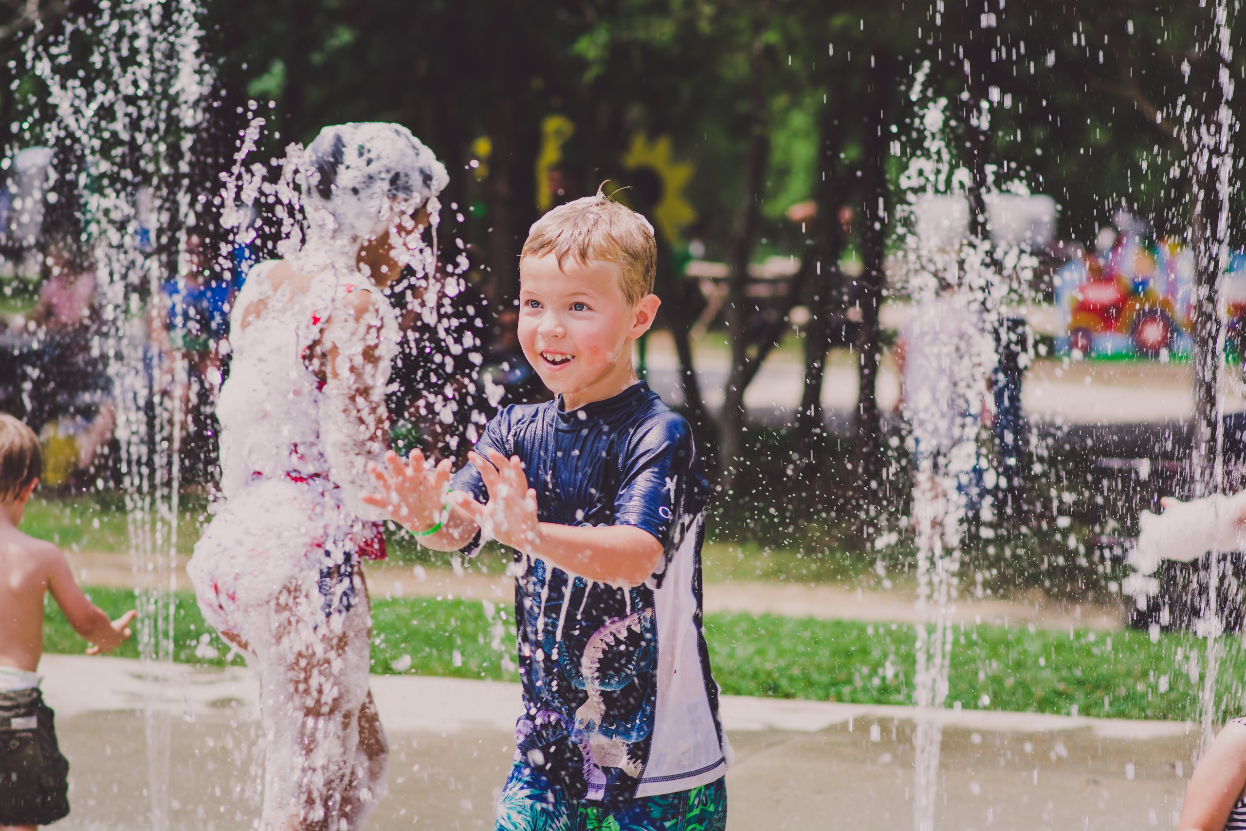 Children joyfully play in a water fountain on a sunny day, getting soaked and laughing in Williamson County, Tennessee.