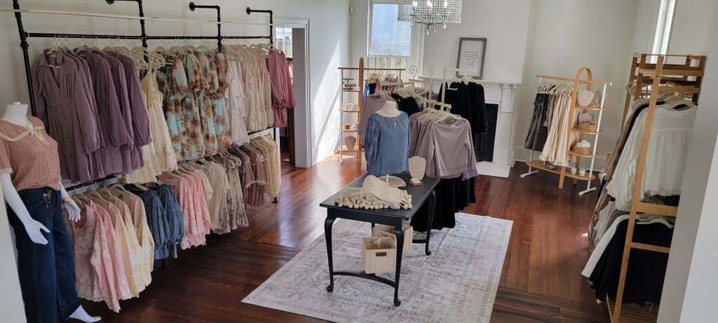 A charming boutique with a variety of women's clothing displayed on racks and mannequins, featuring a cozy ambiance with hardwood floors, a chandelier, and a fireplace in Williamson County, Tennessee.
