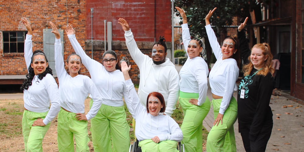 A diverse group of dancers in white tops and bright green pants perform an energetic routine outdoors, with one member in a wheelchair in Williamson County, Tennessee.