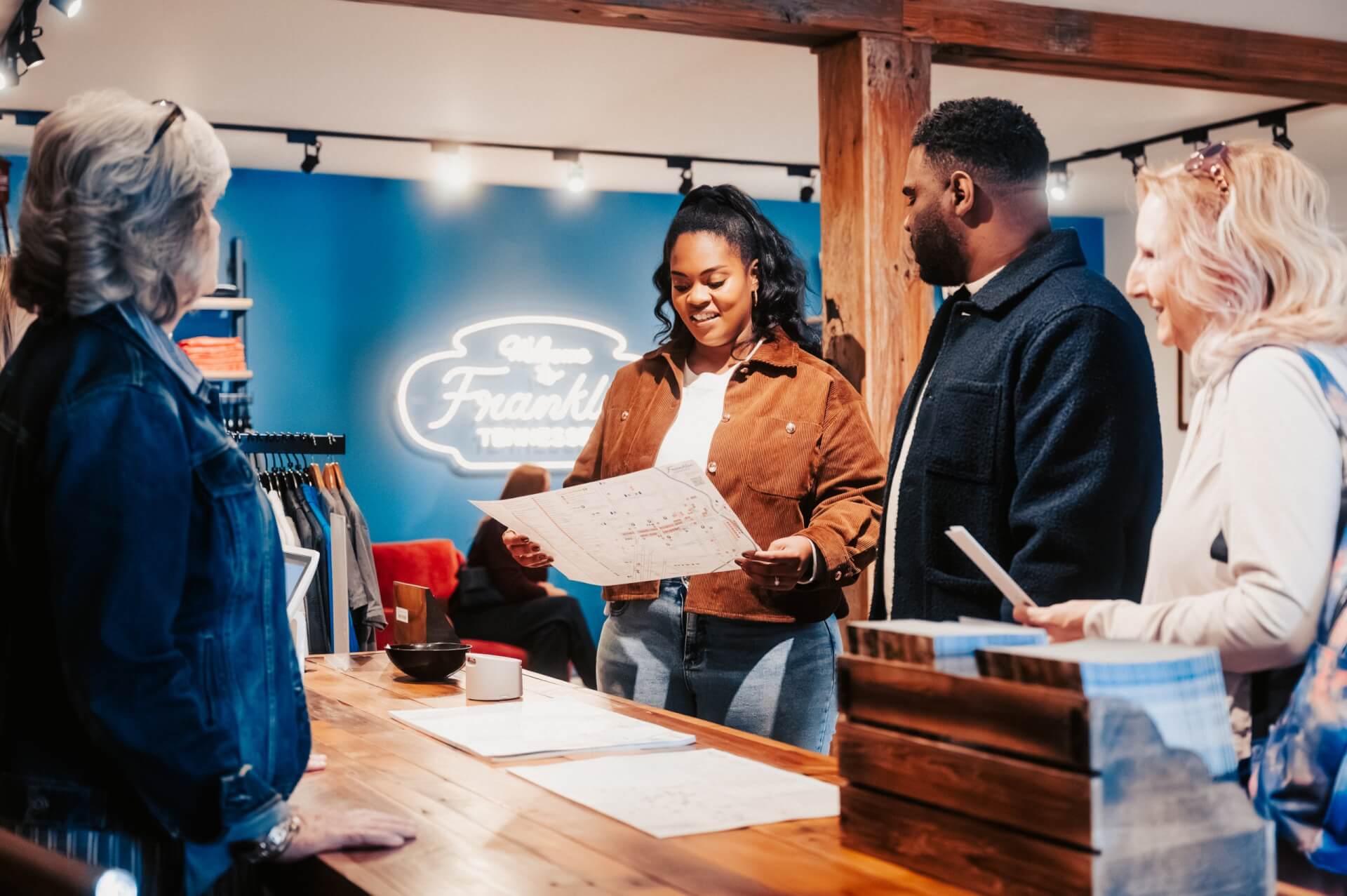 Four people are gathered around a wooden counter in a clothing store, examining a map and discussing their options in Williamson County, Tennessee.
