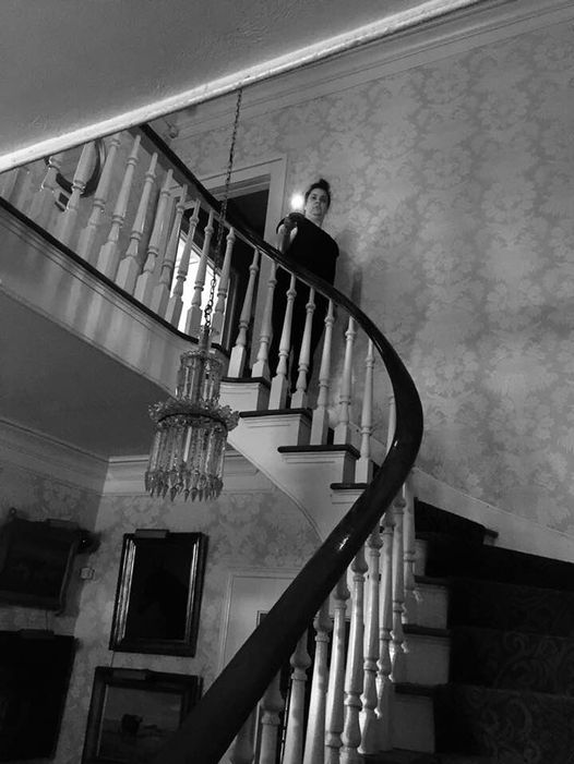 A woman ascends a grand staircase holding a candle, her silhouette framed by ornate railings and a chandelier in Williamson County, Tennessee.