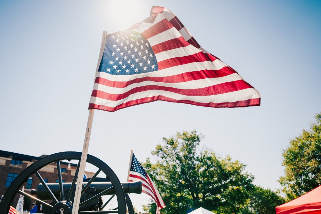 A vibrant American flag waves proudly atop a historic cannon, bathed in warm sunlight against a clear blue sky in Williamson County, Tennessee.