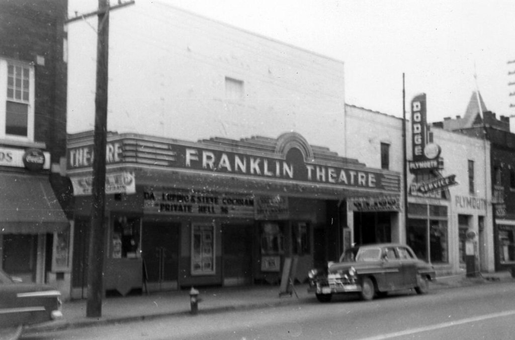 A vintage black and white photograph of the Franklin Theatre in downtown Plymouth, featuring a classic marquee and a parked car from the 1950s in Williamson County, Tennessee.