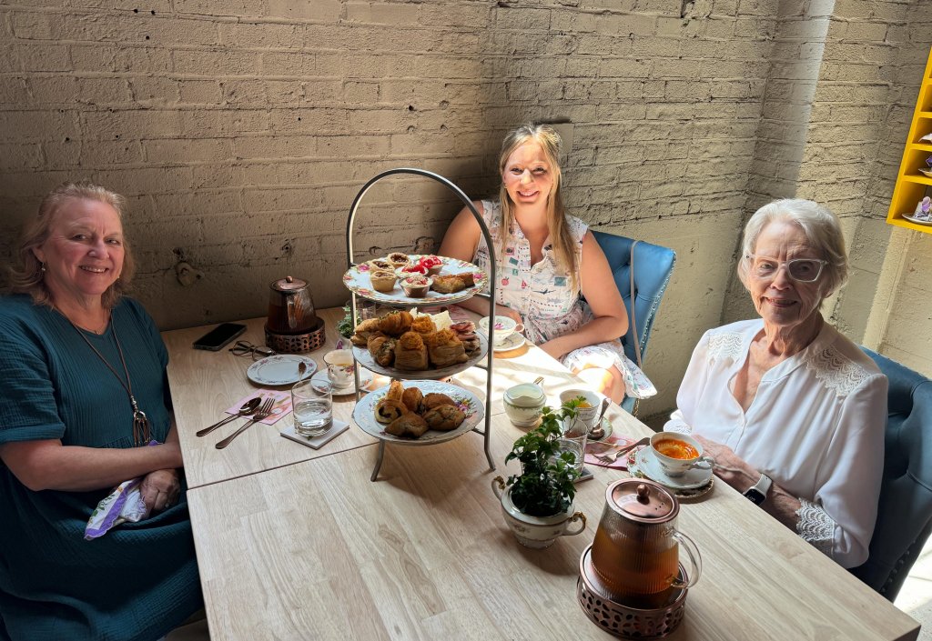 Three women enjoying a traditional afternoon tea with a variety of pastries, sandwiches, and tea in a cozy setting in Williamson County, Tennessee.