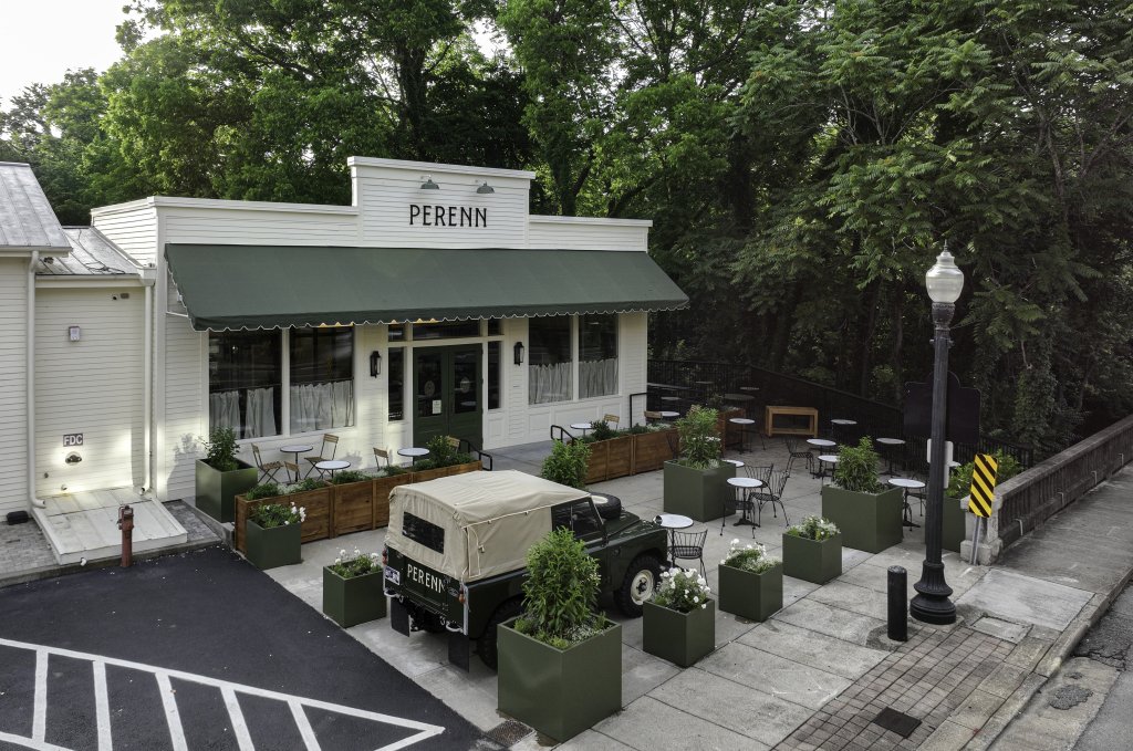 A charming outdoor seating area with green planters and tables at a restaurant named PERENN, featuring a vintage green truck parked in front in Williamson County, Tennessee.