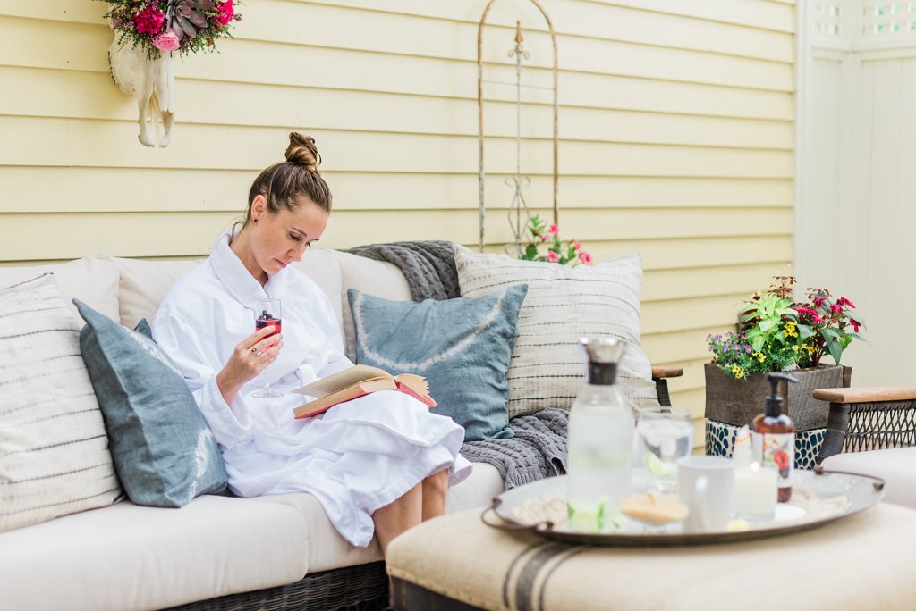 A woman in a white robe relaxes on a cozy outdoor sofa, sipping wine and reading a book in Williamson County, Tennessee.