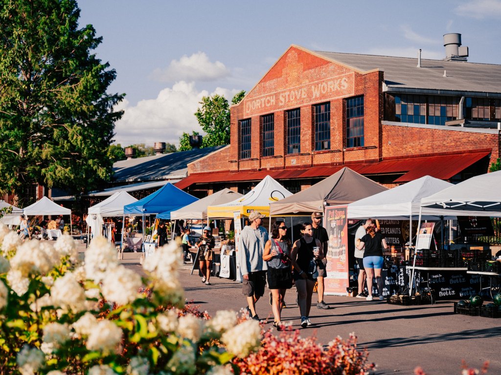 A bustling outdoor market with colorful tents and people shopping under a clear blue sky, with a historic brick building in the background in Williamson County, Tennessee.