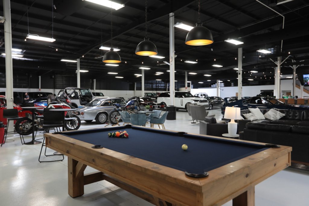 A spacious indoor car showroom with a pool table, lounge area, and various vehicles on display in Williamson County, Tennessee.