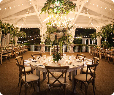 An elegant outdoor wedding reception under a canopy of string lights, featuring round tables with white linens, wooden chairs, and lush floral centerpieces in Williamson County, Tennessee.