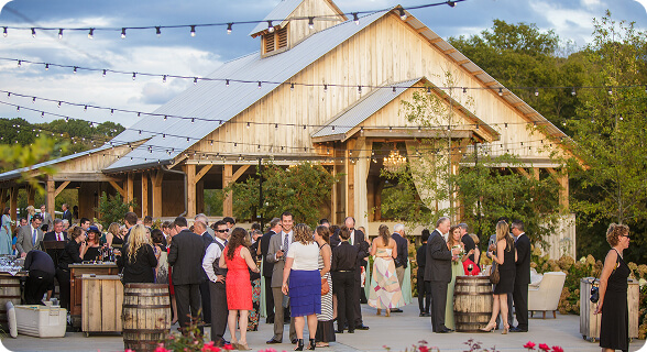 Guests mingle at an outdoor wedding reception under string lights at a rustic wooden barn in Williamson County, Tennessee.