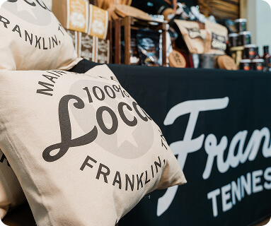 A display of branded merchandise including pillows and a tablecloth featuring the name 'Franklin, Tennessee' and the word 'Loco' in a stylish font in Williamson County, Tennessee.