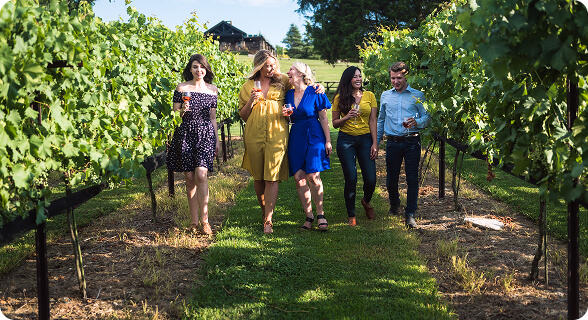 Five friends enjoying a sunny day, walking through a lush vineyard with glasses of wine in hand in Williamson County, Tennessee.