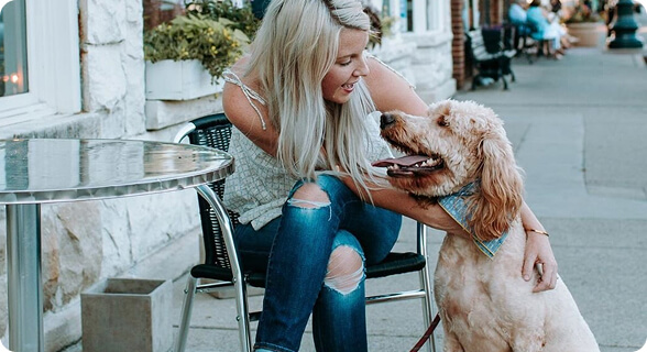 A woman with long blonde hair is sitting on a chair outside a cafe, petting her friendly golden dog in Williamson County, Tennessee.
