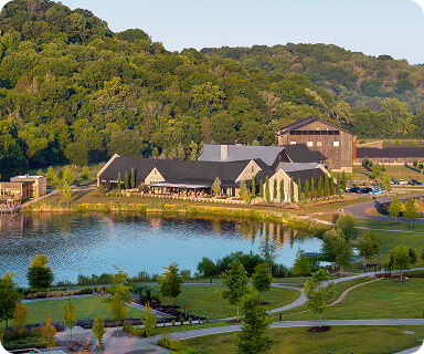 A serene lakeside community nestled among lush green hills, featuring a large building with a gray roof and multiple windows, surrounded by well-manicured lawns and winding pathways in Williamson County, Tennessee.