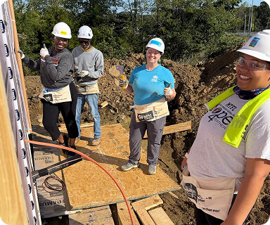 A group of five construction workers, all wearing hard hats and safety vests, stand together smiling at a construction site with a partially built wall and exposed foundation in Williamson County, Tennessee.