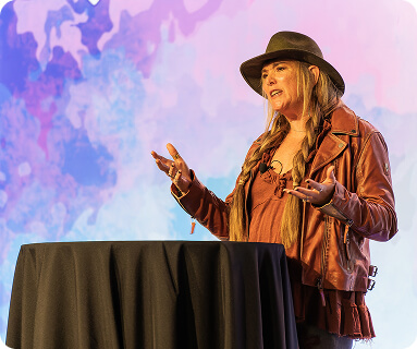 A woman wearing a brown leather jacket and hat gestures expressively while speaking at a podium covered with a black cloth in Williamson County, Tennessee.