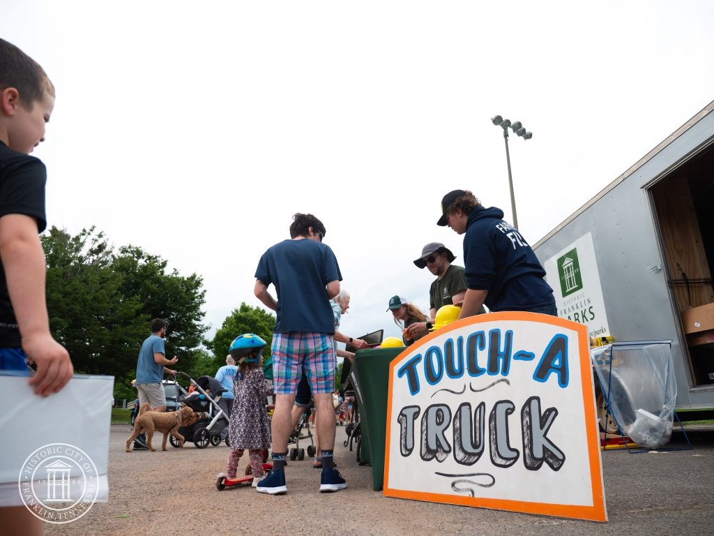 A community event with a 'Touch-A-Truck' sign, where children and adults interact with various vehicles and equipment in Williamson County, Tennessee.
