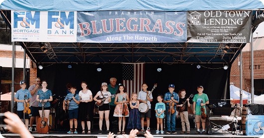 Bluegrass Along the Harpeth A group of children and adults perform bluegrass music on stage at a community event in Williamson County, Tennessee.