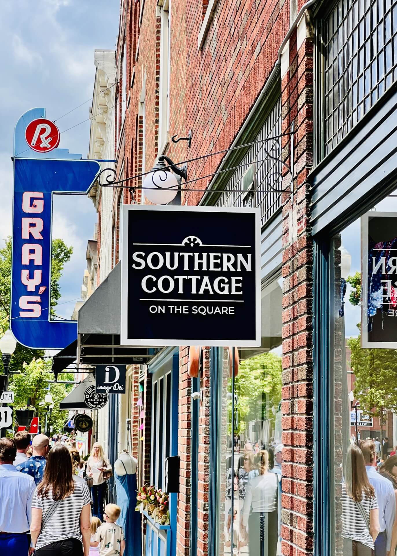 Southern Cottage A bustling street scene in a historic district, featuring a variety of shops with vintage signage, including 'Southern Cottage on the Square' and 'Gray's', with pedestrians strolling along the sidewalk in Williamson County, Tennessee.