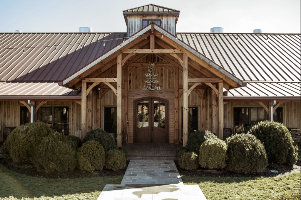 International Tennessee Whiskey Day at Leiper’s Fork Distillery A rustic wooden barn with a metal roof, surrounded by manicured hedges and a stone pathway leading to the entrance in Williamson County, Tennessee.