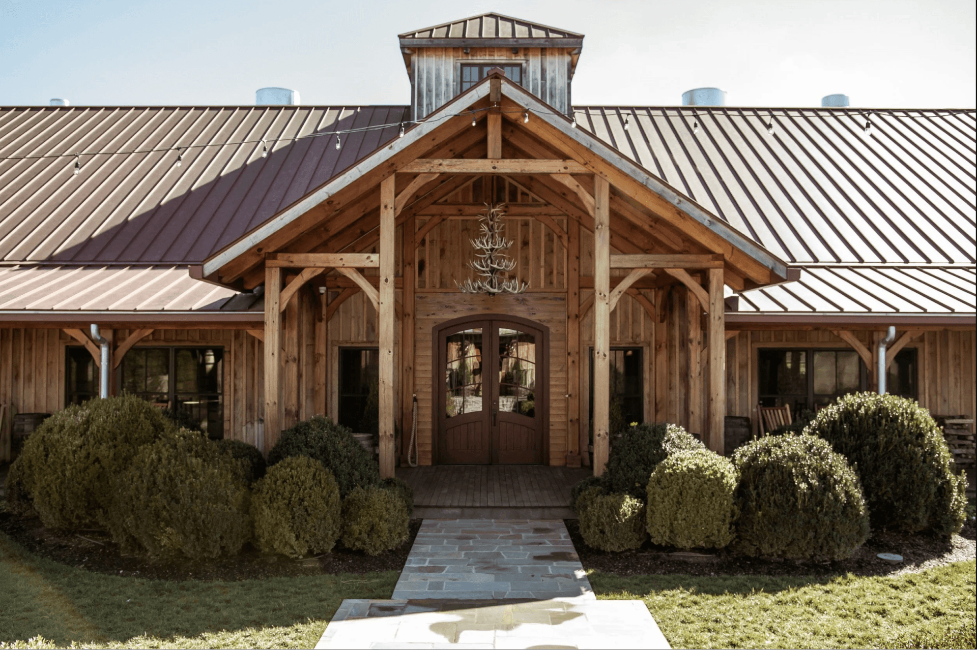 International Tennessee Whiskey Day at Leiper’s Fork Distillery A rustic wooden barn with a metal roof, surrounded by manicured hedges and a stone pathway leading to the entrance in Williamson County, Tennessee.