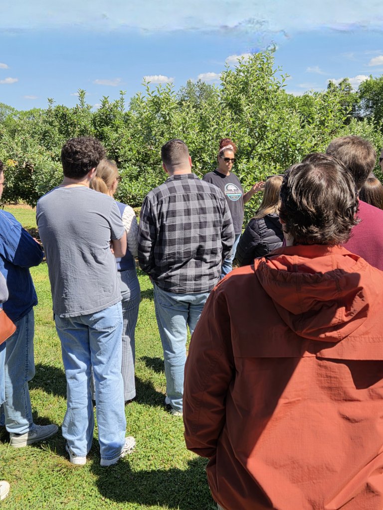 Events A group of people is gathered outdoors, listening to a speaker in an apple orchard under a clear blue sky in Williamson County, Tennessee.