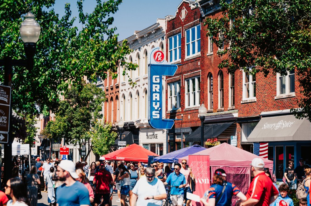 A bustling downtown street filled with people shopping and dining under colorful umbrellas on a sunny day in Williamson County, Tennessee.